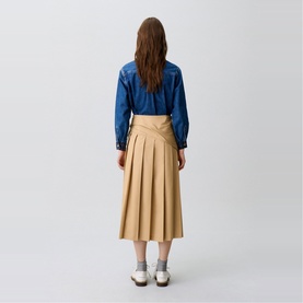 Model wearing Claude Pierlot Pleated Drape Skirt in clear beige with midi length and side pleats, styled with a denim shirt and white shoes.