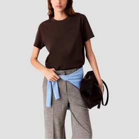 Model wearing Maje dark brown short-sleeve crew neck T-shirt with small logo detail, styled with grey wide-leg trousers and blue shirt tied at waist
