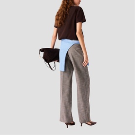 Model carrying Maje dark brown suede clutch bag with top handle, styled with grey wide-leg trousers and brown tee