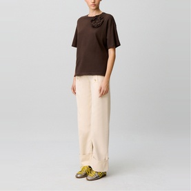 Model wearing Claude Pierlot brown short-sleeve top with floral neckline detail, styled with cream wide-leg trousers and yellow trainers.