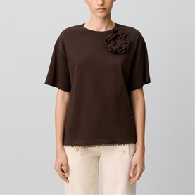 Model wearing Claude Pierlot brown short-sleeve top with floral rosette appliqu&eacute; and scalloped lace hem, styled with cream trousers.