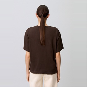 Model wearing Claude Pierlot brown short-sleeve top with lace hem trim, shown from the back, styled with cream trousers.