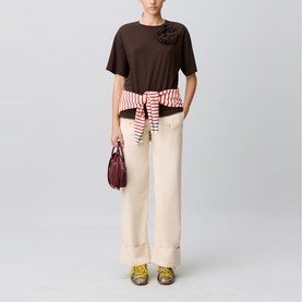Model wearing Claude Pierlot brown short-sleeve top with floral detail, styled with cream wide-leg trousers, red striped tie belt, and carrying a