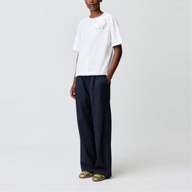 Model wearing Claude Pierlot white short-sleeve T-shirt with chest embellishment, styled with wide-leg navy trousers and yellow sandals.