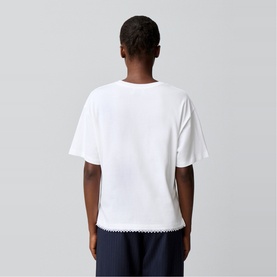 Model wearing Claude Pierlot white T-shirt, back view, with scalloped navy hem trim, styled with navy trousers.