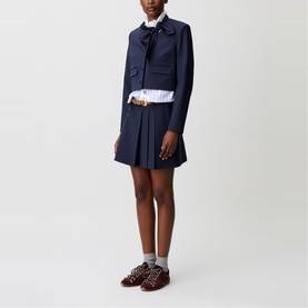 Model wearing Claude Pierlot Cropped Single-Breasted Blazer in blue with matching pleated mini skirt, white shirt, and bow collar detail.