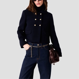 Model wearing Maje navy double-breasted cropped jacket with gold buttons, styled with dark denim jeans, chain belt and burgundy bag