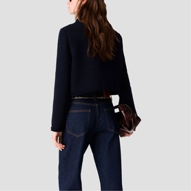 Model wearing Maje navy cropped textured jacket, styled with dark denim jeans and a brown bag, shot from behind.