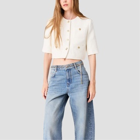Model wearing cream cropped short-sleeve jacket with gold buttons, styled with light blue wide-leg jeans