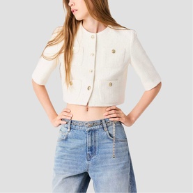 Model wearing cream cropped short-sleeve jacket with gold buttons, styled with light wash embellished jeans