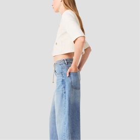 Model wearing wide-leg light blue wash barrel jeans with a white cropped T-shirt, side profile view