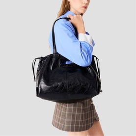 Model carrying Maje red large tote bag with gathered drawstring sides and single shoulder strap, styled with blue top and check mini skirt