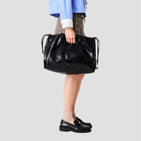 Model carrying Maje red bag with drawstring top detail and structured silhouette, styled with checked skirt and black loafers