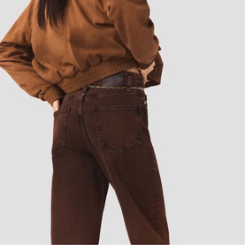 Model wearing Maje brown straight-leg jeans with a brown bomber jacket and dark chain belt, rear view