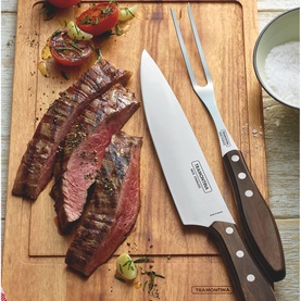 Tramontina cutlery set with carving knife and fork, dark wood handles, displayed on wooden board with sliced grilled steak