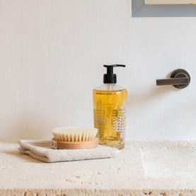 BAOBAB Hand Wash amber liquid pump bottle styled on stone surface with natural bristle brush and folded cloth