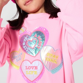 Model wearing Billy Blush pink dress with iridescent heart patches reading Love Life and Stay Cool, long sleeves, relaxed fit