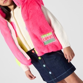 Model wearing Billy Blush pink fluffy gilet with neon yellow hem, styled with cream knit jumper and denim skirt with coloured buttons.