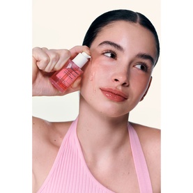 Model with Biodance serum held to cheek, shown in pink ribbed top, highlighting glowing skin application
