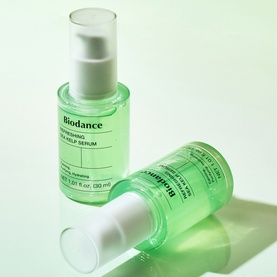 Biodance serum in green glass pump bottle, shown upright and on its side against a light green background