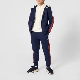 Model wearing navy zip-up hoodie with red and white side panels, matching joggers, cream knit, and dark trainers