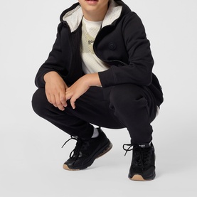 Model wearing black zip-up hoodie with cream sherpa lining, styled with matching black joggers and dark trainers with gum sole