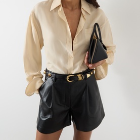 Model with Dehanche Hollyhock Leather Belt in black, gold-tone rounded buckle with tiger eye gemstone detailing, styled with leather shorts.
