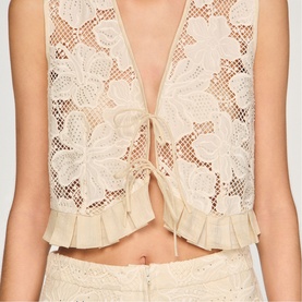 Model wearing Sandro cream lace cropped top with deep V-neck, tie fastening, and frill hem, styled with matching lace skirt