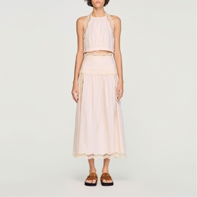 Model wearing Sandro light pink halterneck crop top and midi skirt co-ord with gold trim detail, styled with brown strappy sandals.