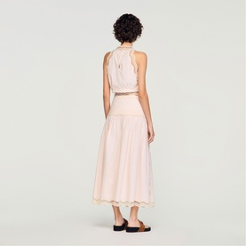 Model wearing Sandro light pink sleeveless halterneck midi dress with scallop hem detailing, shown from behind