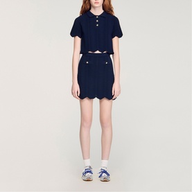 Model wearing Sandro navy blue scallop-hem mini skirt and matching cropped polo top, styled with white socks and blue trainers.