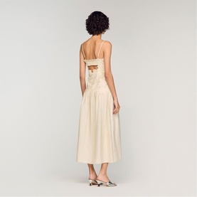 Model wearing Sandro Womens French Dress in clear, open-back midi silhouette with thin straps, styled with silver mules, back view