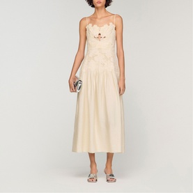 Model wearing Sandro Womens French Dress in clear, midi length with floral appliqu&eacute; bodice and full skirt, styled with silver sandals and clutch bag.