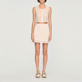 Model wearing Sandro crochet mini skirt in clear pink, styled with matching crop top and gold sandals