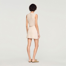 Model wearing Sandro crochet mini skirt in clear/cream, styled with matching sleeveless crochet top and nude flat mules, rear view.