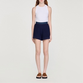 Model wearing Sandro navy blue pleated shorts with white sleeveless top and brown strappy sandals
