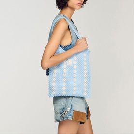 Model carrying Sandro sky blue crochet tote bag with white floral detail, styled with denim top and shorts