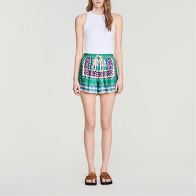 Model wearing Sandro green and purple embroidered shorts with white sleeveless top and brown flat sandals