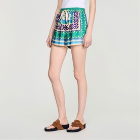 Model wearing Sandro green and purple printed shorts with tie waist, styled with tan suede sandals