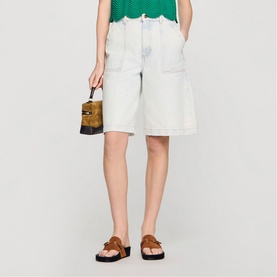 Model wearing light blue denim shorts, carrying a small printed box bag, with Sandro brown open-toe strappy sandals with chunky sole.