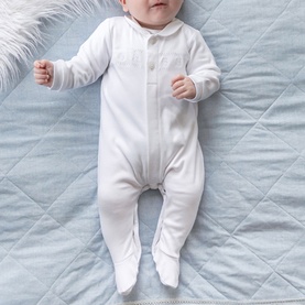 Emile Et Rose white baby all-in-one sleepsuit with footed legs and front button detail, worn by infant on quilted surface