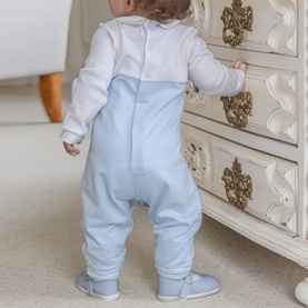 Model wearing Emile Et Rose pale blue all-in-one with white top, viewed from behind, standing at an ornate white dresser.