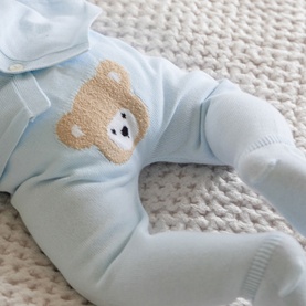 Emile Et Rose pale blue baby all-in-one with textured bear motif on chest, shown flat on cream knit blanket