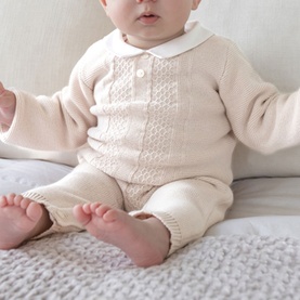 Emile Et Rose stone knit baby all-in-one with white collar, cable-knit front detail and button placket, seated pose