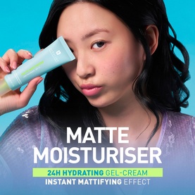 Model with Erborian Matte Moisturiser 24H Hydrating Gel-Cream tube held to face, shown against bright blue background.