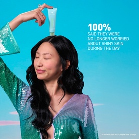 Model with Erborian Matte Moisturiser tube held above head, wearing a teal sequin jacket, against a blue background
