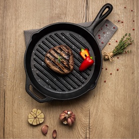 Tramontina Black cast iron grill pan with ridged base, styled with a grilled burger patty, red pepper, garlic and herbs on a wooden surface.
