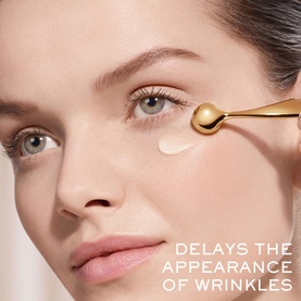 Model with Lanc&ocirc;me skincare eye serum, gold roller applicator dispensing cream beneath eye, with text: Delays the Appearance of Wrinkles