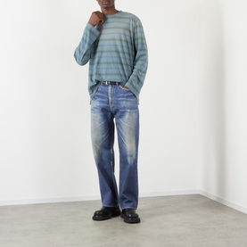 Model wearing Our Legacy Azure Print jeans in faded blue denim, styled with a striped knit jumper and black loafers