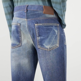Model wearing Our Legacy Azure Print jeans, close-up of rear view showing faded wash, five-pocket styling and brown leather patch detail.
